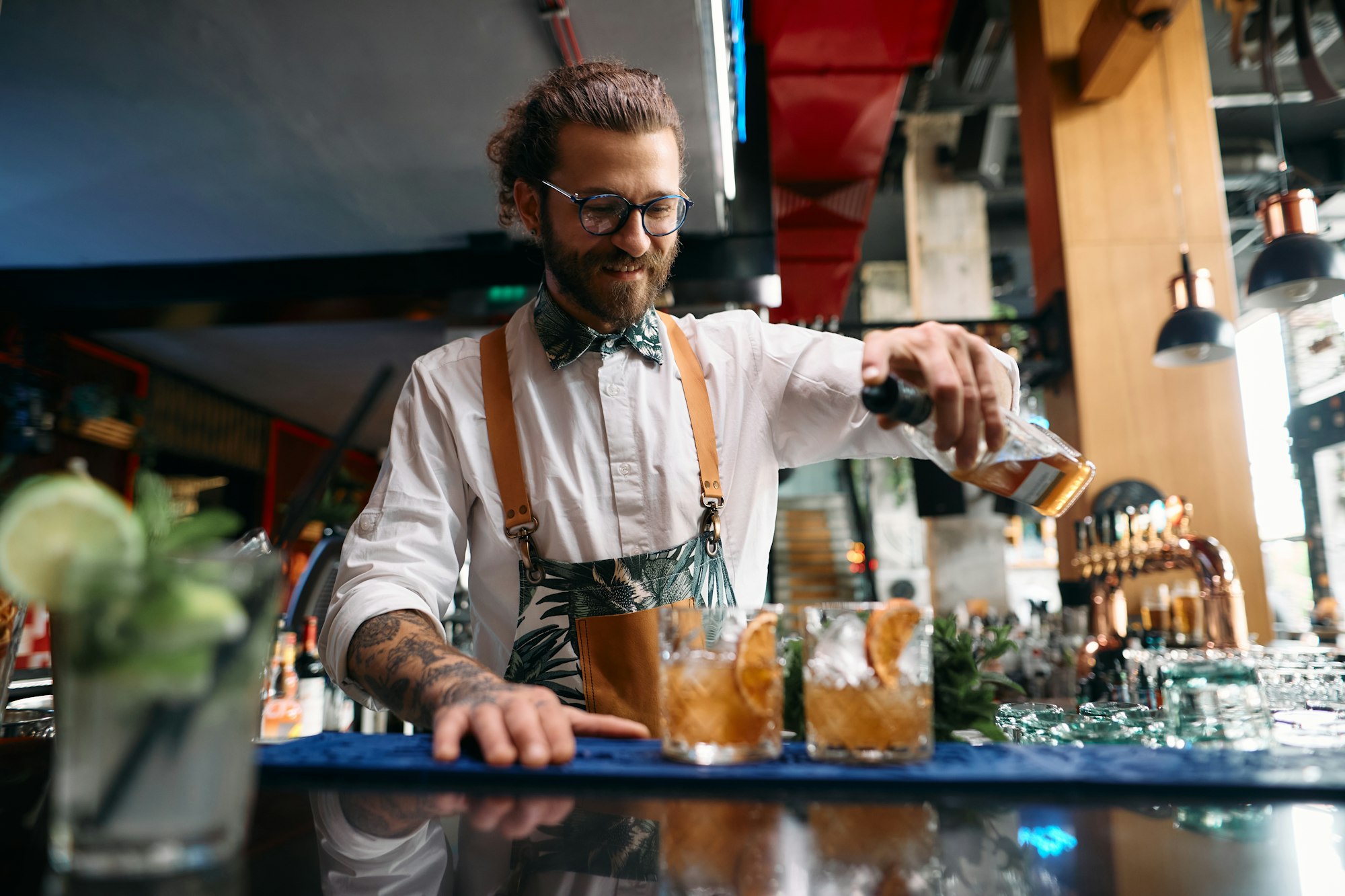 Happy barista preparing cocktails at bar counter in night club.